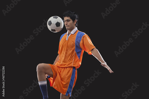 Male football player doing kick ups isolated over black background