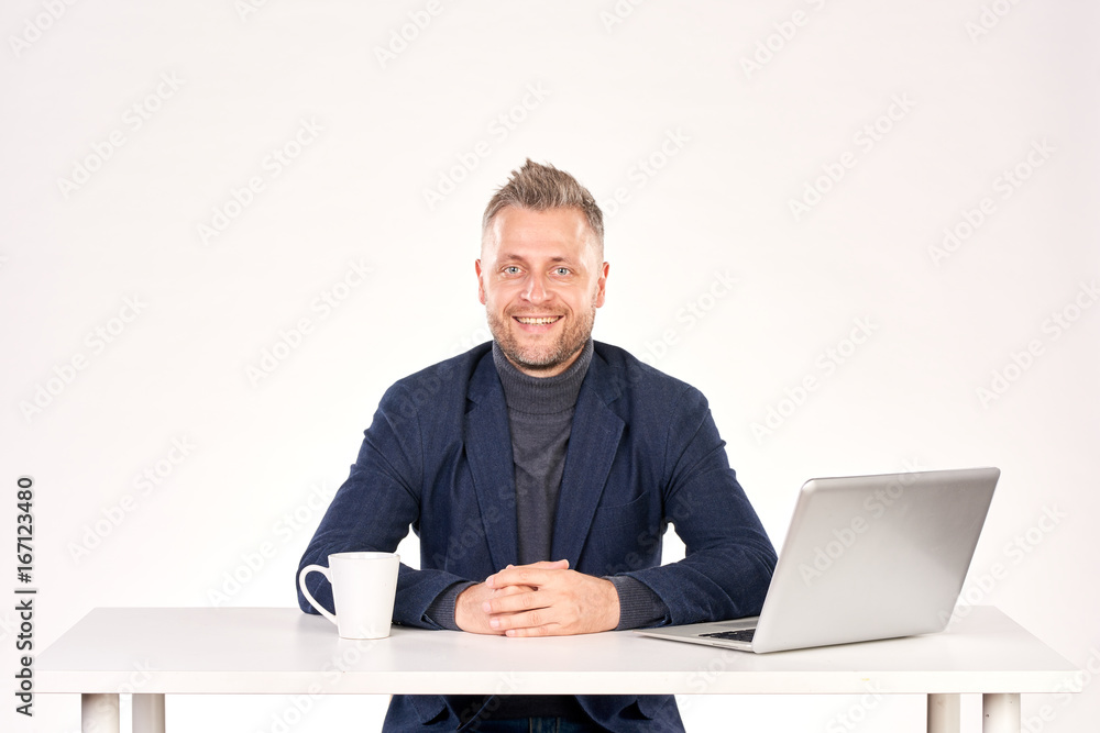 Portrait of middle-aged businessman sitting at office desk with laptop on it Portrait of middle-aged businessman sitting at office desk with laptop on it