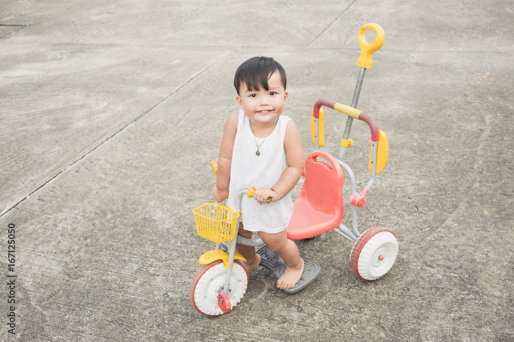 Cheerful of baby stand on kid's bicycle and looking camera on concrete road background. Copy space Cheerful of baby stand on kid's bicycle and looking camera on concrete road background. Copy space