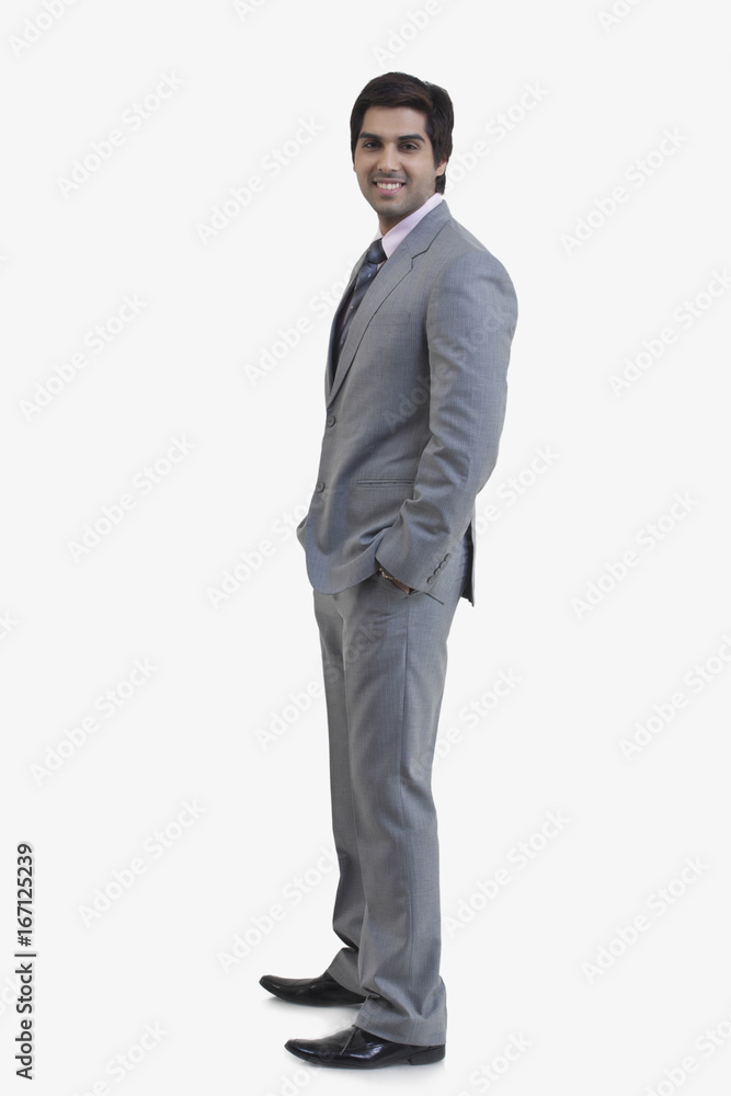 Side view of young businessman with hands in pockets standing against white background Side view of young businessman with hands in pockets standing against white background