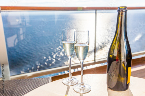 Champagne bottle and flutes glasses on luxury cruise travel for honeymoon holidays. Boat at sea on vacation sunset with celebration drinks. photo