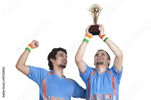 Happy young male friends in jerseys cheering up with winning trophy over white background 