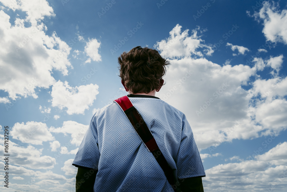 Low angle rear view of boy standing against cloudy sky Low angle rear view of boy standing against cloudy sky