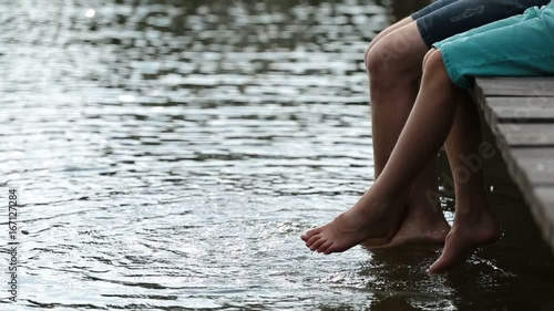 Father and son dangling legs into water and splash