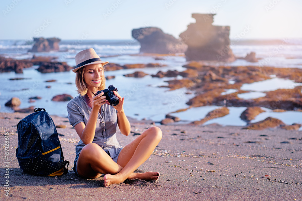 Travel and hobby. Pretty young woman with camera and rucksack on the ocean beach.