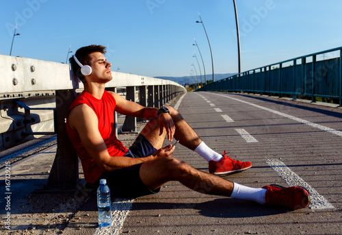 Portrait of young athlete man resting after running and drinking water on bridge.