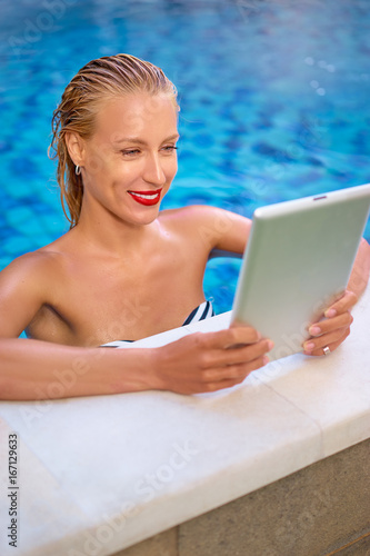 Vacation and technology. Pretty young woman using tablet computer in swimming pool.
