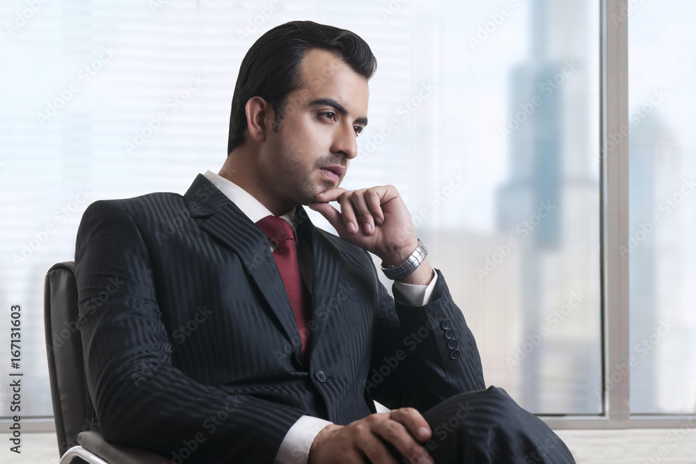Thoughtful businessman sitting by window in office Thoughtful businessman sitting by window in office