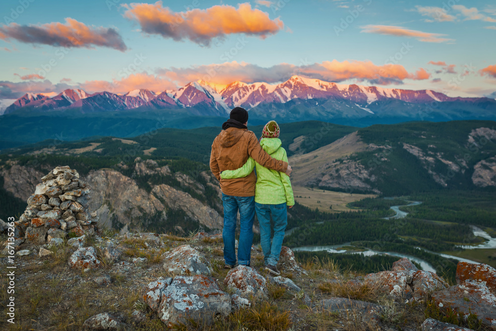 Tourist couple - girl and guy embracing and enjoying beautiful mountain landscape with morning haze over the mountains and forests. Panorama
