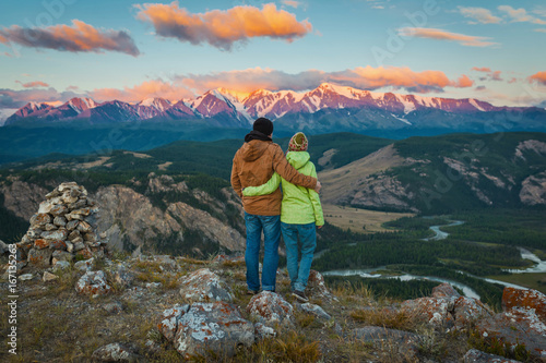 Tourist couple - girl and guy embracing and enjoying beautiful mountain landscape with morning haze over the mountains and forests. Panorama