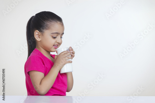 Cute girl drinking glass of milk against white background