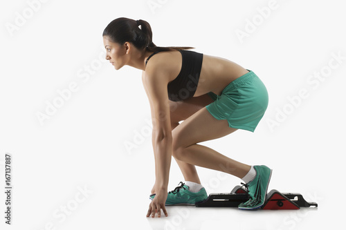Profile shot of young female runner at starting block isolated over white background