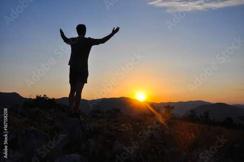 Silhouette of man resting and watch sunrise high into a mountain. Concept of happiness and summer vacations, Looking at the sun