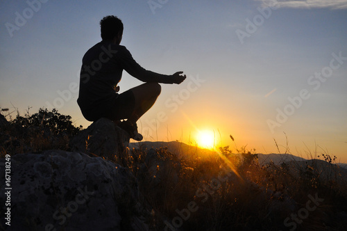 Silhouette of man meditating in sitting yoga position on the top of a mountains. Man meditate on mountain at sunrise