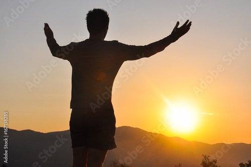 Silhouette of man resting and watch sunrise high into a mountain. Concept of happiness and summer vacations, Looking at the sun © Ivan