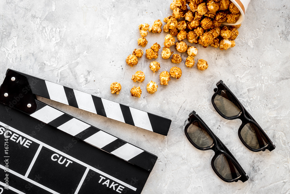 Watching film in the cinema. Clapperboard, glasses and popcorn on grey background top view copyspace