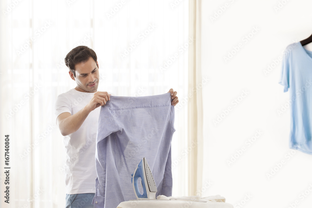 Young man looking at shirt with ironing board in front Young man looking at shirt with ironing board in front