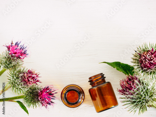 Fotografia burdock oil in small glass bottle and burdock flowers on white wooden table