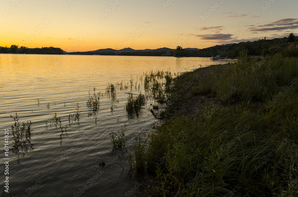 sunset, river view in summer. Colorful landscape summer sunset on the river bank. Sun rays and reflections on water