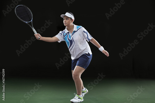 Young female player in sportswear playing tennis over black background © IndiaPix