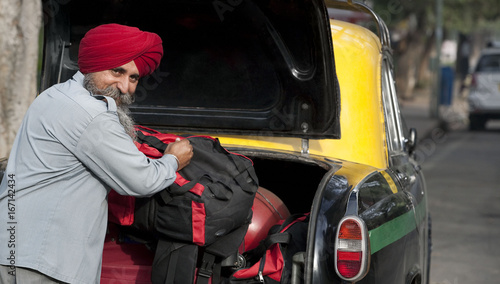 Sikh taxi driver loading luggage into the dickie 