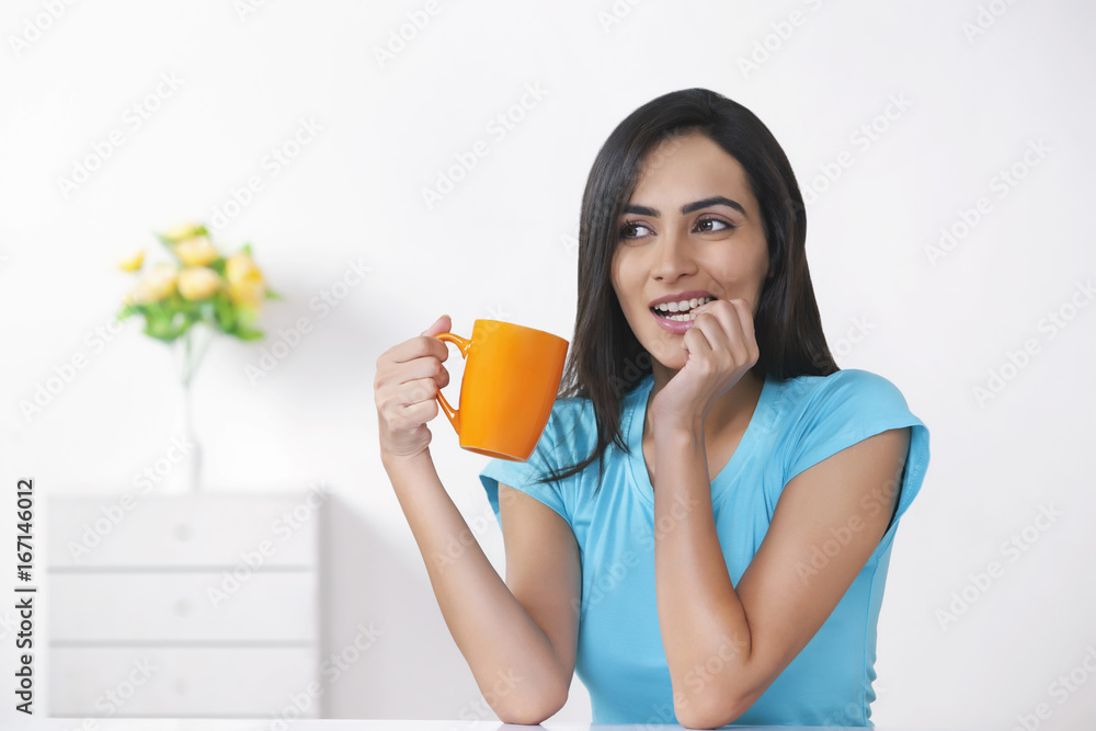Young woman biting nail while holding coffee cup at home Young woman biting nail while holding coffee cup at home