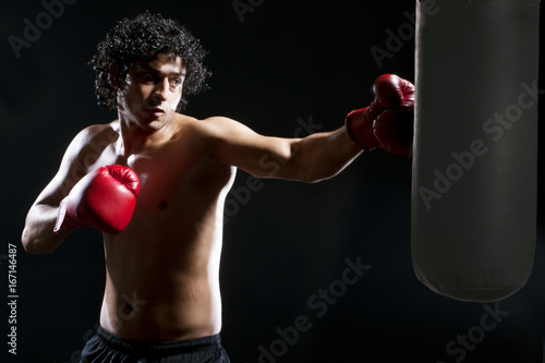 Male boxer hitting heavy bag over black background 