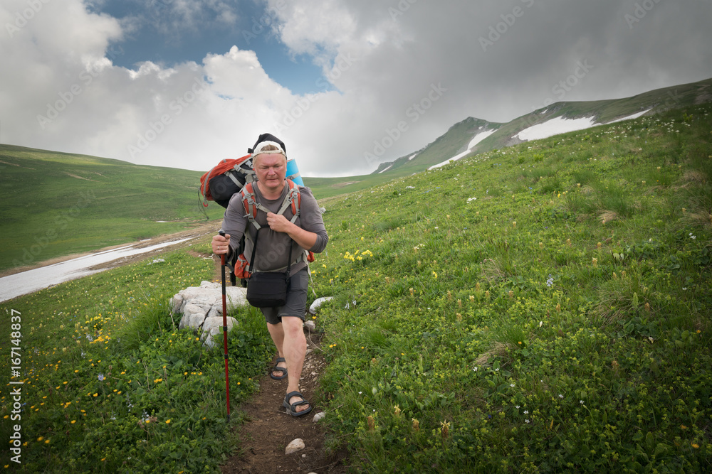 Tourist with a large backpack on a pathway in the mountains