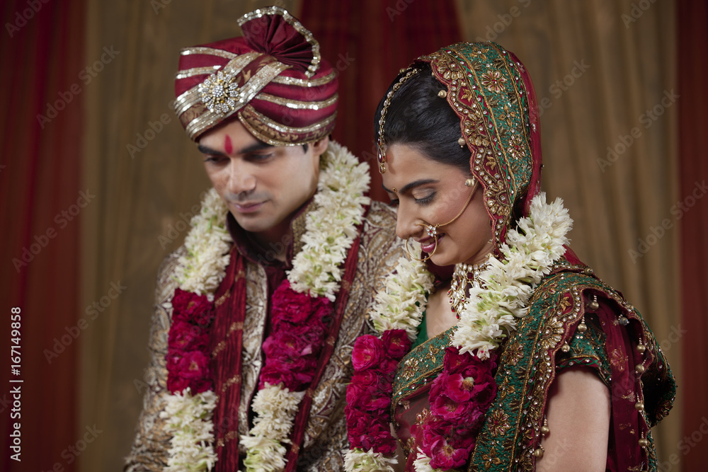 Young couple wearing garlands looking down 