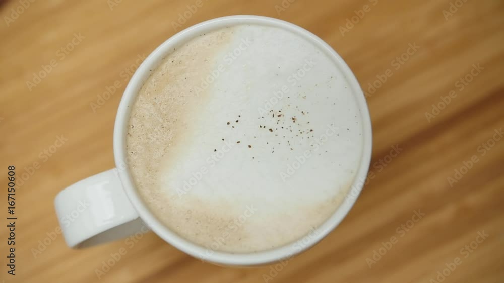 Cup of cappuccino with cinnamon powder on the bar, top view, slow motion. Cup of cappuccino with cinnamon powder on the bar, top view, slow motion.