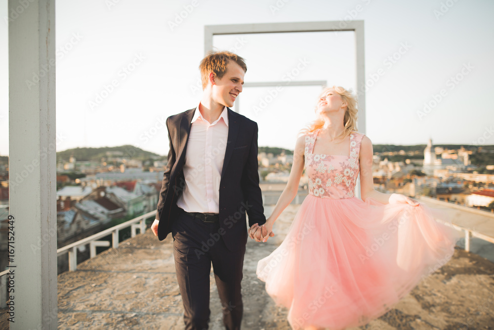 Young loving woman and man walking in city roof holding hands