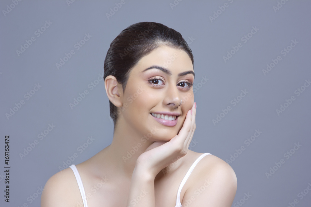 Portrait of smiling young woman touching cheek over blue background Portrait of smiling young woman touching cheek over blue background