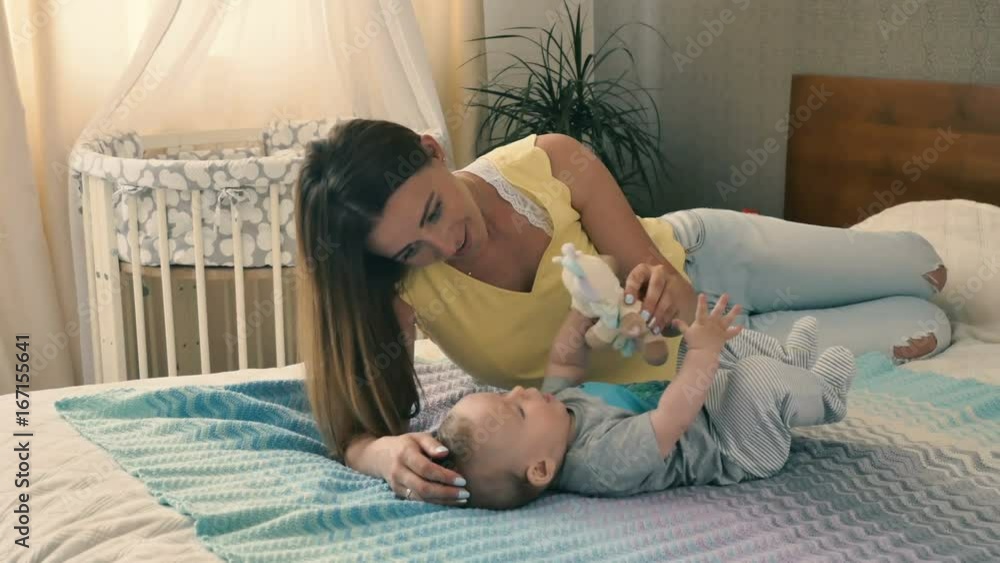 Lovely mother plays soft toy with her baby at the bed Lovely mother plays soft toy with her baby at the bed
