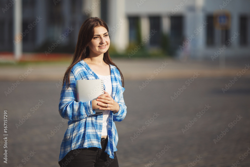 Young cute student woman with books in hands standing in morning light on university building background. Campus life, holiday, education concept