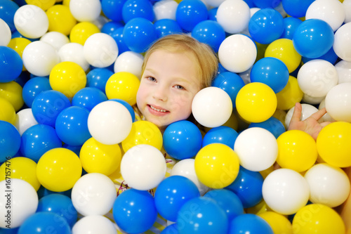 Happy little girl having fun in ball pit in kids indoor play center. Child playing with colorful balls in playground ball pool. photo