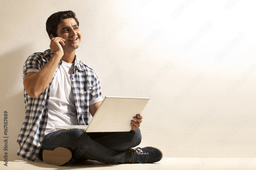 Handsome young man with laptop talking on cell phone Handsome young man with laptop talking on cell phone