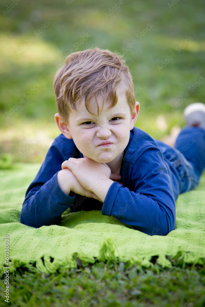 Young boy pulling grumpy face while laying on blanket outdoors Young boy pulling grumpy face while laying on blanket outdoors