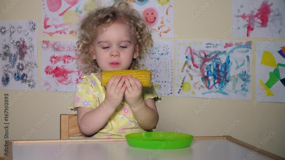 Young funny girl eating a boiled corn sitting by table at home Young funny girl eating a boiled corn sitting by table at home