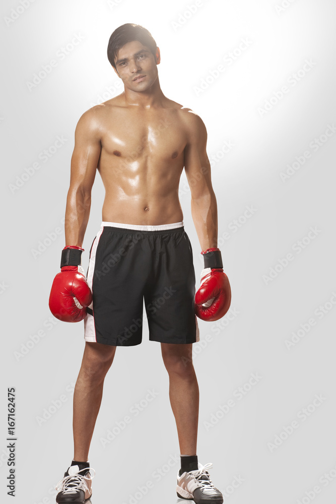 Full length portrait of shirtless boxer wearing boxing gloves against white background Full length portrait of shirtless boxer wearing boxing gloves against white background