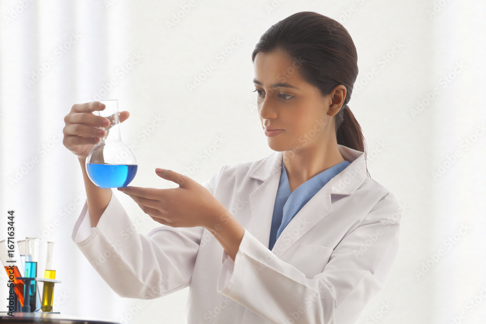 Young female scientist looking at liquid in beaker Young female scientist looking at liquid in beaker