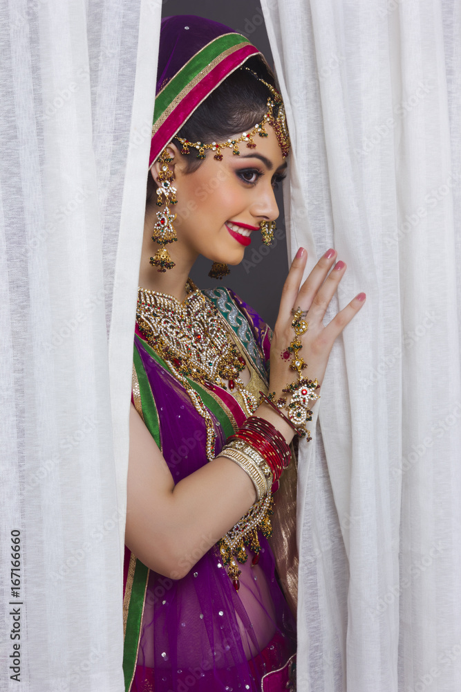 Shy Indian bride standing amidst curtains