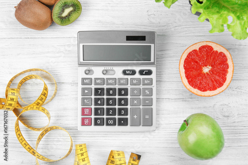 Diet concept. Calculator, measuring tape and different groceries on wooden background