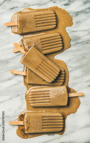 Summer healthy vegan frozen dessert. Flatlay of melting coffee latte popsicles over light grey marble background, top view