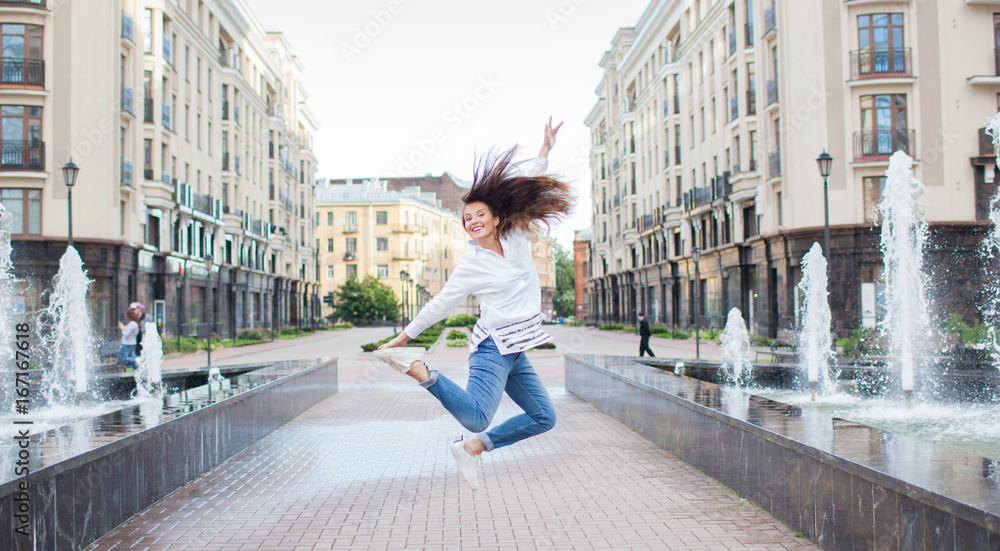 Young sporty girl jumping for joy at the fountain in the residential complex. Female in flight with his hands up