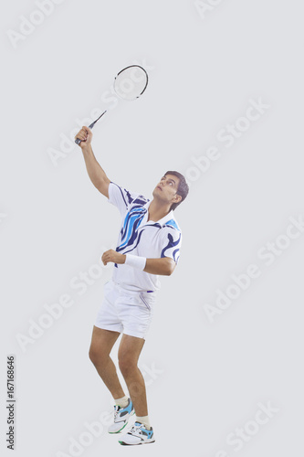 Full length of young man in sports wear playing badminton isolated over gray background
