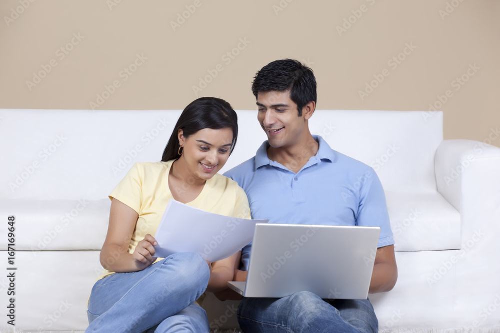 Young couple looking at document while using laptop Young couple looking at document while using laptop