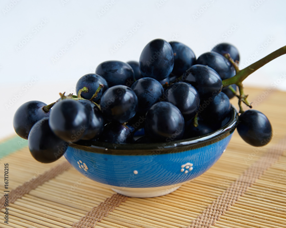 A bunch of black grapes in a blue cup A bunch of black grapes in a blue cup