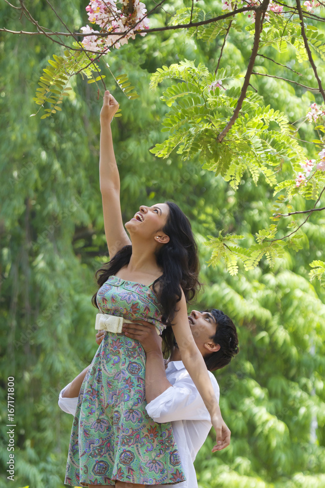 Man helping woman reach for branch of tree Man helping woman reach for branch of tree