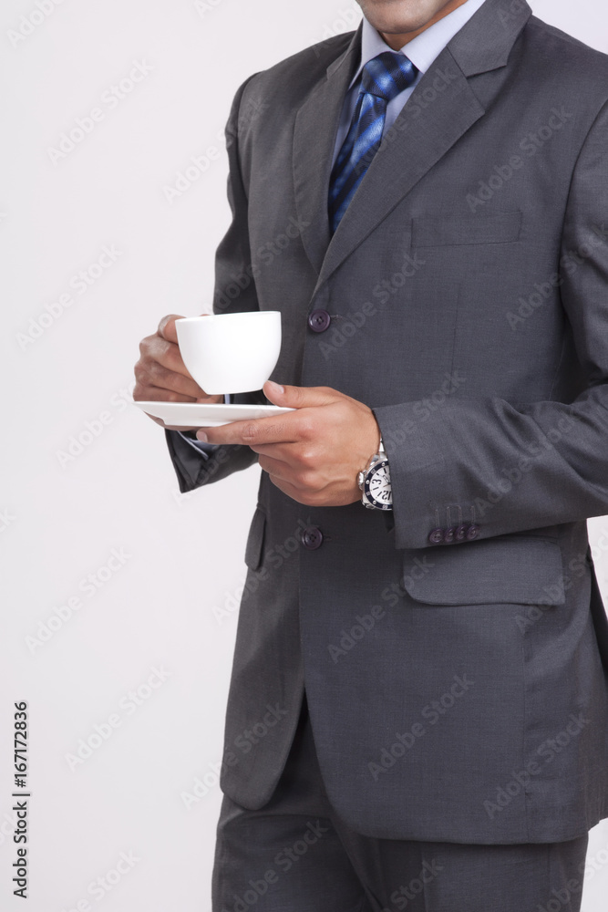 Midsection of businessman holding coffee cup against gray background Midsection of businessman holding coffee cup against gray background