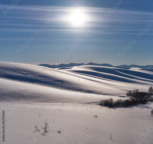 Winter landscape with heels under snow with Sun on blue sky